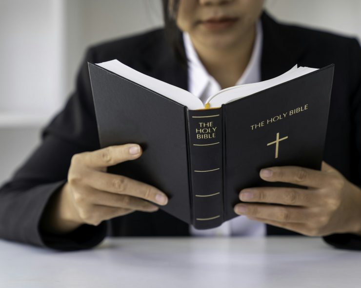 Christian woman holds bible in her hands. Reading the Holy Bible in a field during beautiful sunset.