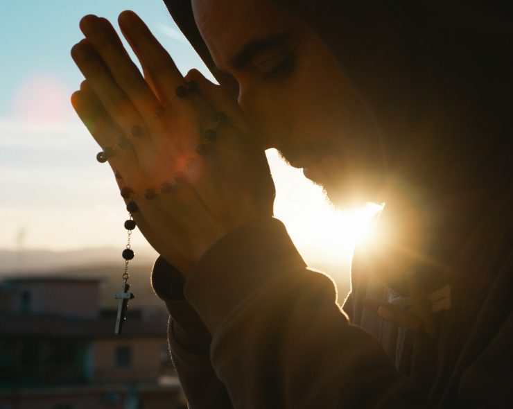 Silhouette of praying man with christian crucifix